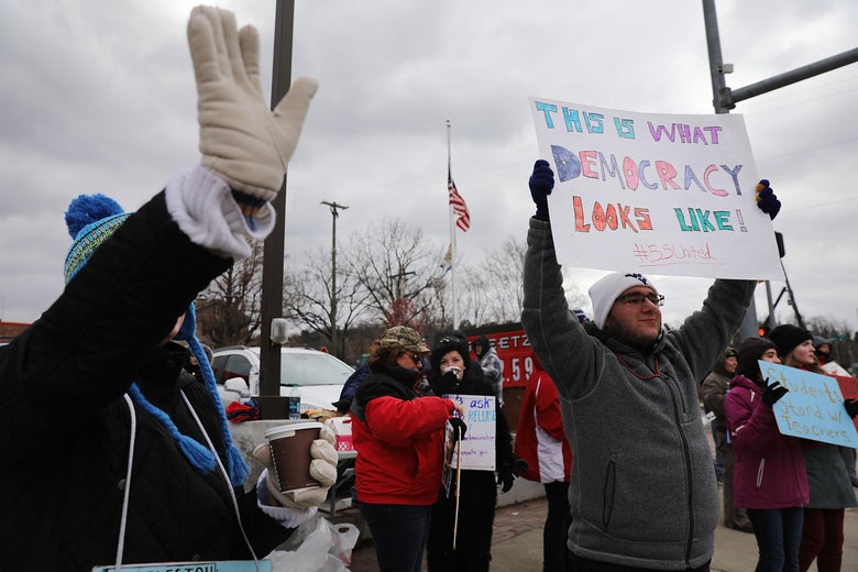 West Virginia teachers, students, and supporters hold signs on a street.